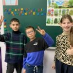 Three children in front of a blackboard in a classroom